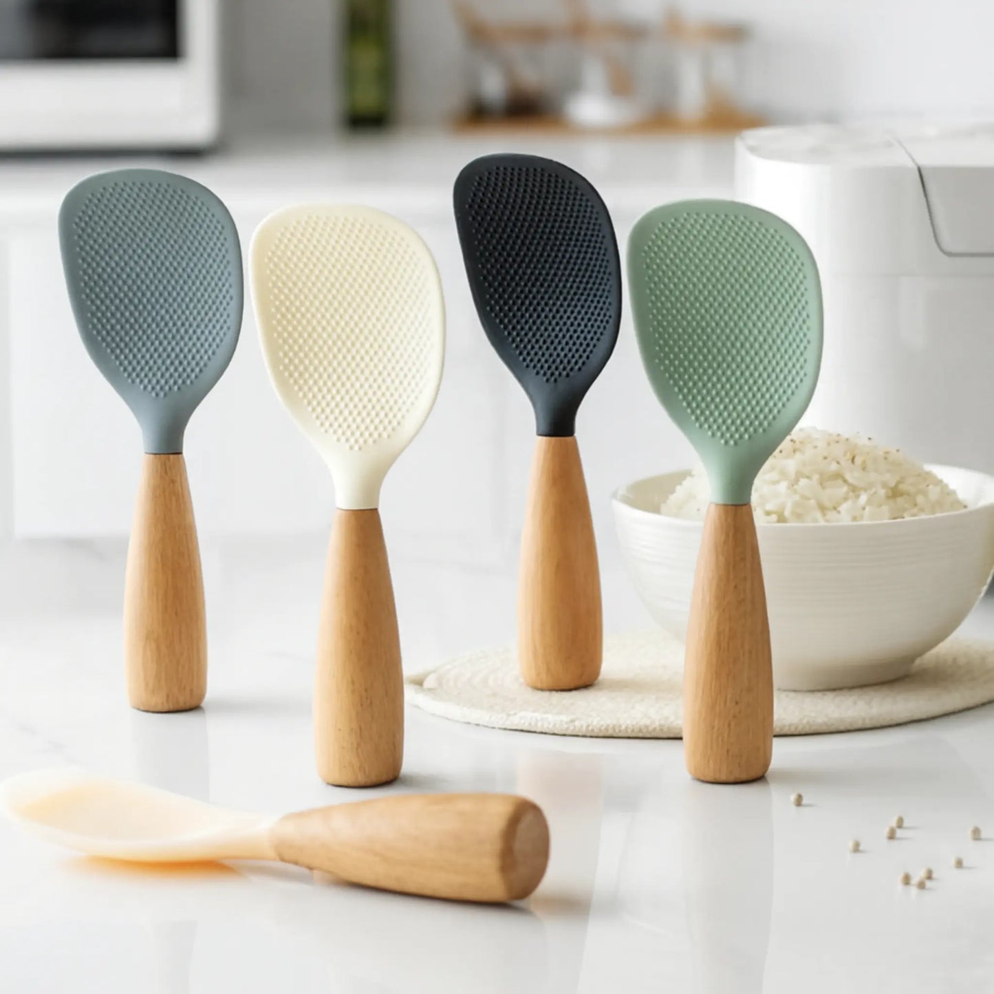 Four kitchen utensils with wooden handles and silicone heads on a kitchen counter.